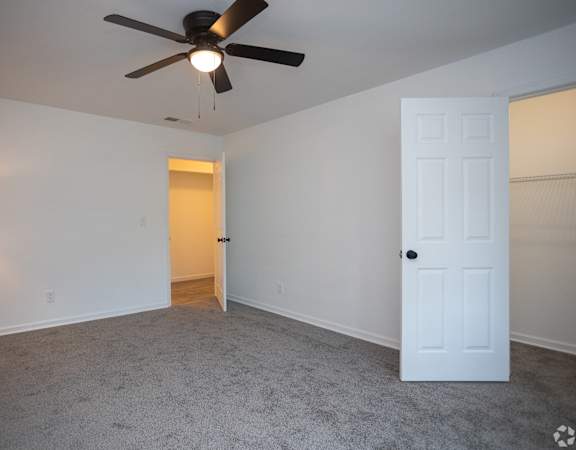 an empty living room with a ceiling fan and a white door