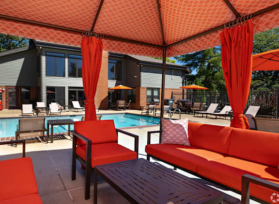 A poolside seating area with red cushions and umbrellas.