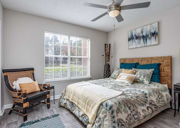 Furnished apartment bedroom with a large window and ceiling fan inside a model unit at Waters Edge at Harbison 