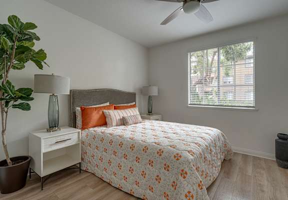 A bedroom with a bed, nightstand, and a plant.