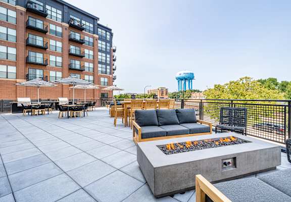 a patio with a fire pit and chairs and tables and a building in the background