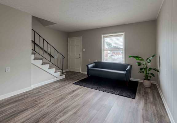 an empty living room with a black couch and a staircase