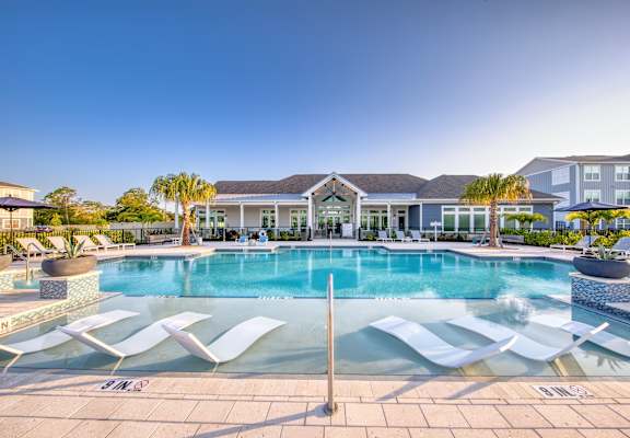 A large swimming pool with lounge chairs and a building in the background.