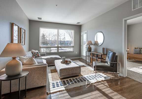 A living room with a grey couch, a black chair, and a round mirror on the wall.