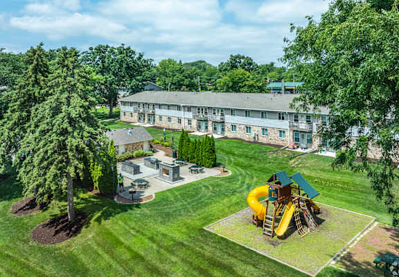 A playground with a yellow slide is surrounded by a green lawn and trees.