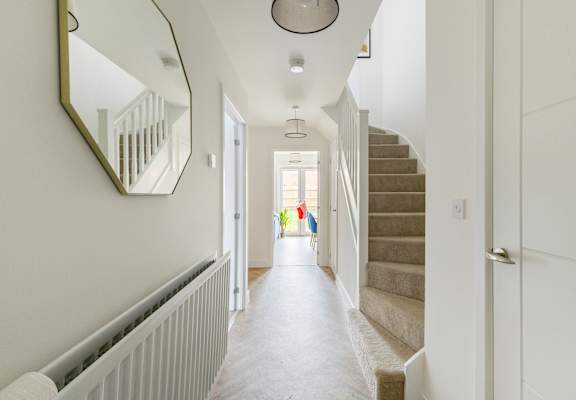 A hallway with a staircase and a mirror on the wall.