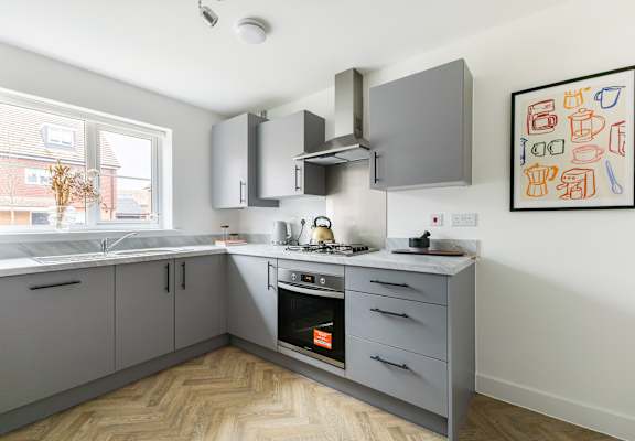 A modern kitchen with a wooden floor and grey cabinets.