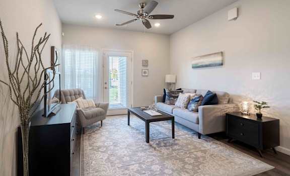 A living room with a grey couch, a black side table, and a ceiling fan.