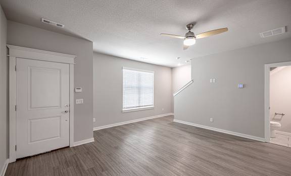 an empty living room with a white door and a ceiling fan