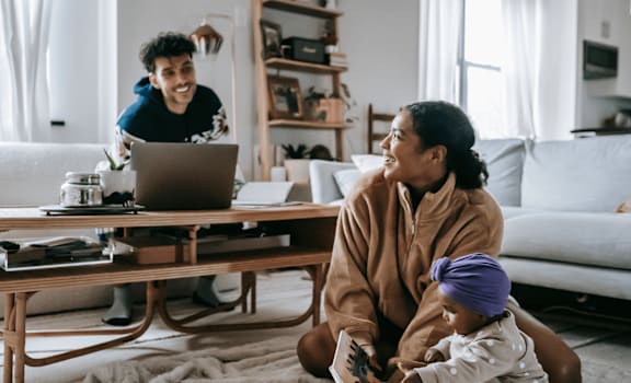 A woman and a child are sitting on the floor in front of a coffee table with a laptop open.