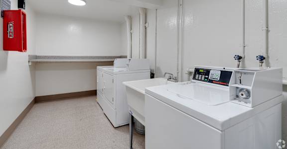 A clean, white room with a red fire extinguisher on the wall and a white machine with a digital display in the center.