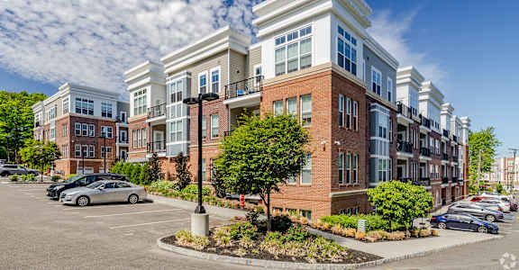 A row of modern townhouses with a parking lot in front.