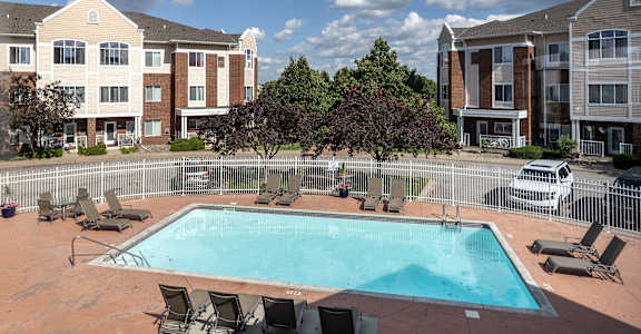 A swimming pool surrounded by chairs and trees in front of apartment buildings.