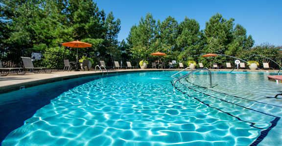 A large swimming pool with a blue tinted water and a sun umbrella.