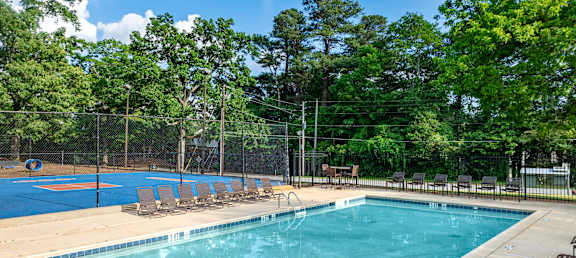 A large outdoor swimming pool surrounded by trees and a fence.