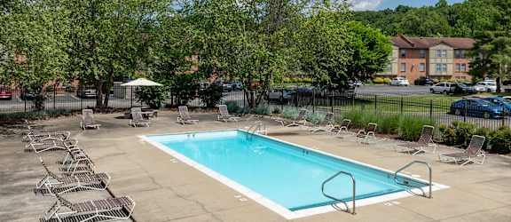 a swimming pool with chairs and trees and a building in the background