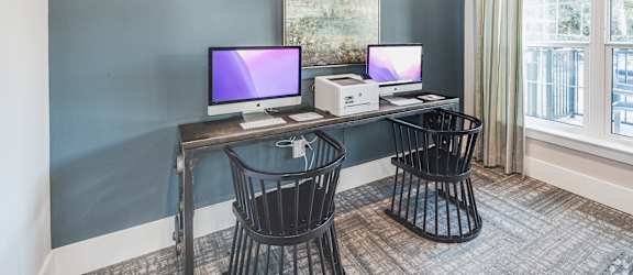 two computers sitting on a desk in a room with two chairs