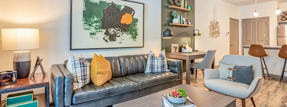 A living room with a grey couch and a painting on the wall.