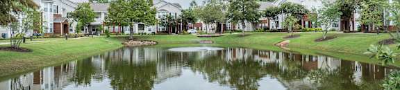 a pond with houses in the background and grass and trees at Carlton Park Apartment Homes, Flowood, Mississippi