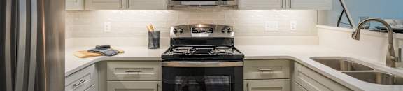 a kitchen with white cabinets and a stove and a microwave at The Vineyard at Castlewoods Apartment Homes in Mississippi 39047