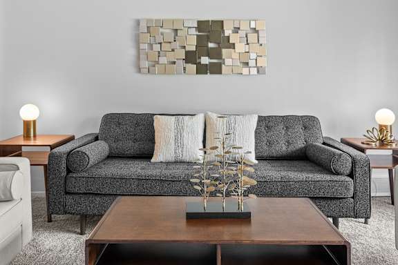 A grey couch with pillows and a wooden coffee table in the middle of the room.