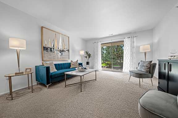 A living room with a blue couch and a painting of sailboats on the wall.