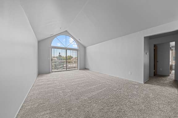 A room with a large carpet and a window with a view of a fence and trees.