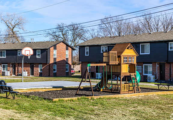 A playground with a basketball hoop and a wooden swing set. at Blacklark Apartments, Apartments, Kansas City, KS