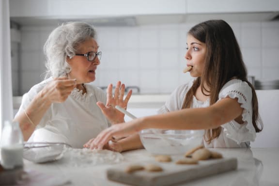 two women sitting at a table in a kitchen making cookies