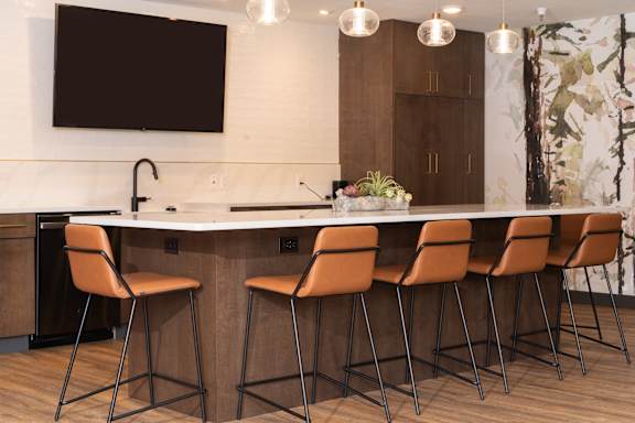 A kitchen with a white counter and brown chairs.