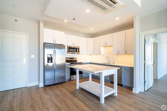 a kitchen with white cabinets and stainless steel appliances and a white island with three chairs