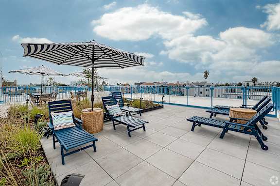 A patio with blue chairs and a striped umbrella.