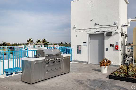 A white building with a blue fence and a grill in front of it.