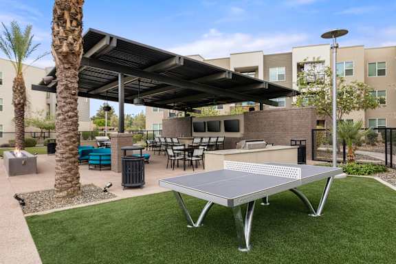 A table tennis table is in the middle of a grassy area.