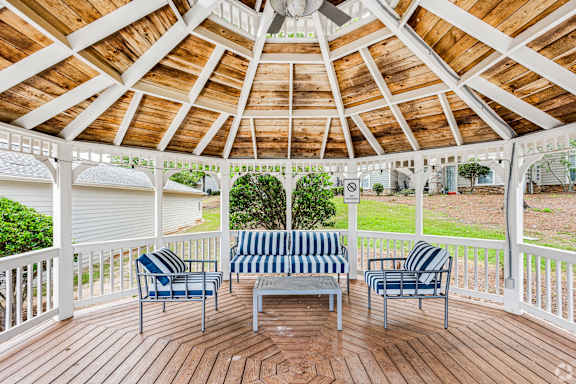 A wooden gazebo with striped cushions on the benches.