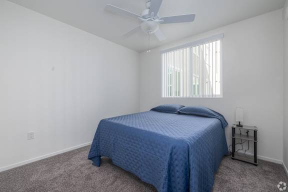 A bedroom with a blue bedspread and a ceiling fan.