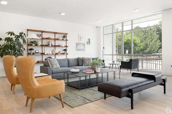 A living room with a grey couch, a wooden chair, a black bench, and a glass table.