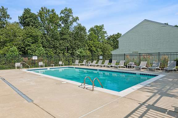 A pool with chairs around it and a building in the background.
