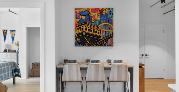 A dining table with four chairs and a painting of a bridge on the wall.