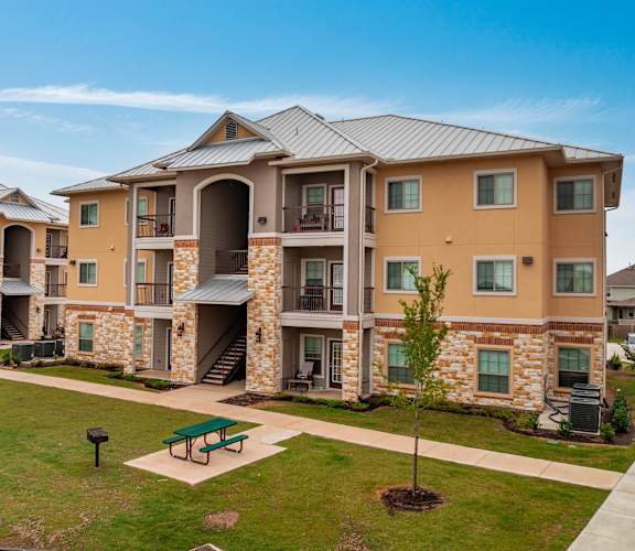 Apartment complex with a green lawn and a tree in front.