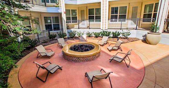 A patio with chairs and a fire pit in the middle of a courtyard.