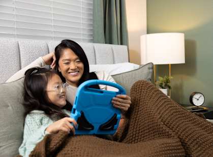 A woman and a girl are sitting on a couch with a blue tablet.