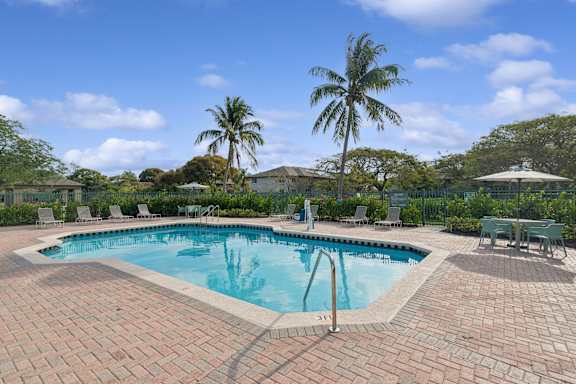 A pool surrounded by a brick patio and palm trees.