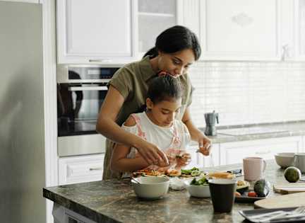 A woman and a child are preparing a meal together in a kitchen.