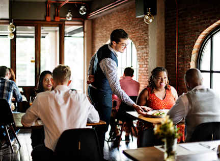 A waiter is serving food to a group of people in a restaurant.