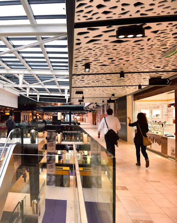 A shopping mall with people walking and escalators.