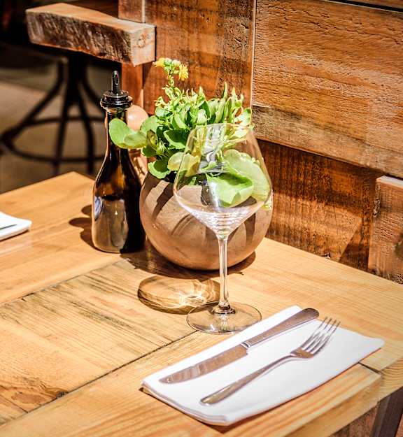 A wooden table with a glass of wine, a bottle, and a vase with a plant.