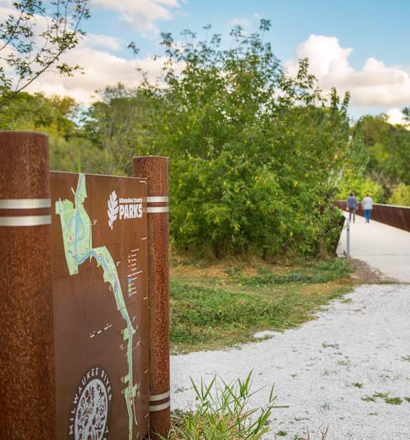 A brown sign with a tree and the word "PARK" on it is on the left side of a gravel path.