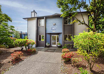 the front of a grey building with a walkway and plants at Eagles Landing Apartments, Everett, WA