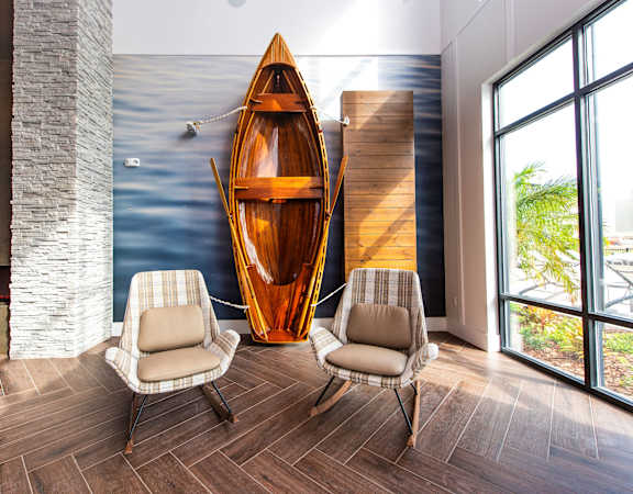 A wooden canoe is on display in a room with two chairs.